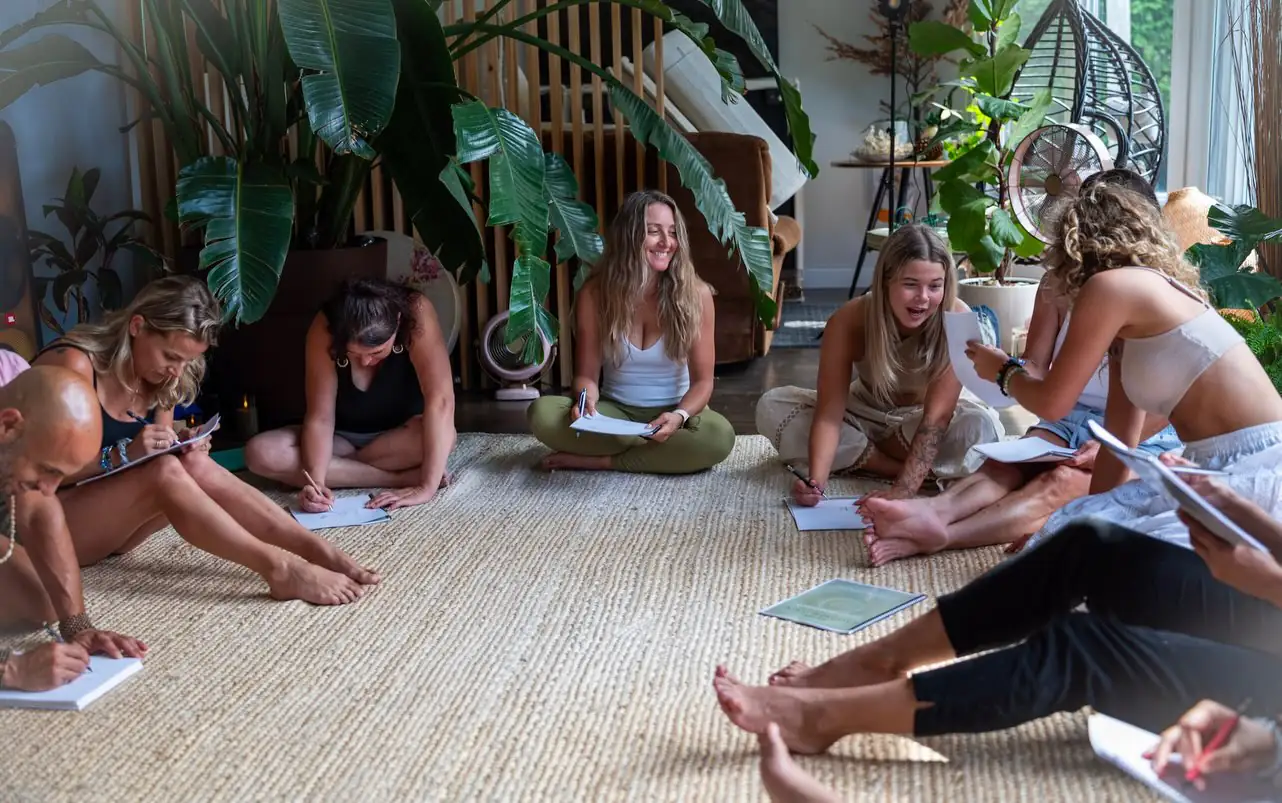 Inside Maison Anahata in Brossard — plants, woven rugs, and a circle gathered on the floor of the main room.